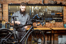 Handsome bearded repairman in workwear serving a sports bike at the bicycle workshop