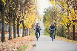 An active senior couple with electrobikes cycling outdoors on a road.